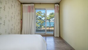 A bedroom with a bed, a window with curtains, and a view of a balcony with a railing. - Tongyeong Haegando Pension (Tongyeong)