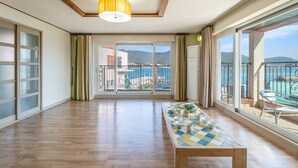 A spacious room with a wooden floor, a checkered table, and large windows offering a view of the sea and mountains. - Tongyeong Haegando Pension (Tongyeong)