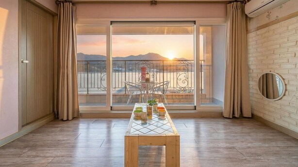 A balcony with a table set for four, a view of the sunset, and a brick wall. - Tongyeong Haegando Pension (Tongyeong)