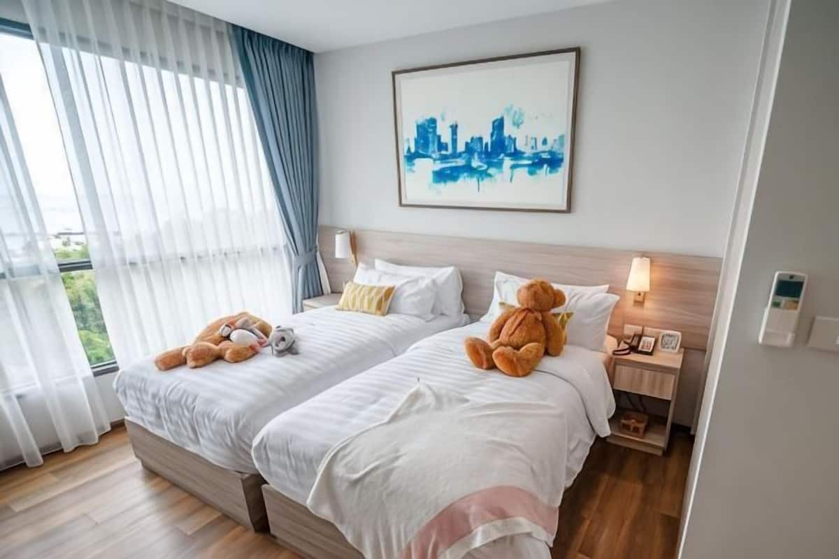 Une chambre d’hôtel avec deux lits, un tableau représentant un paysage urbain, une table de chevet et une fenêtre avec des rideaux.