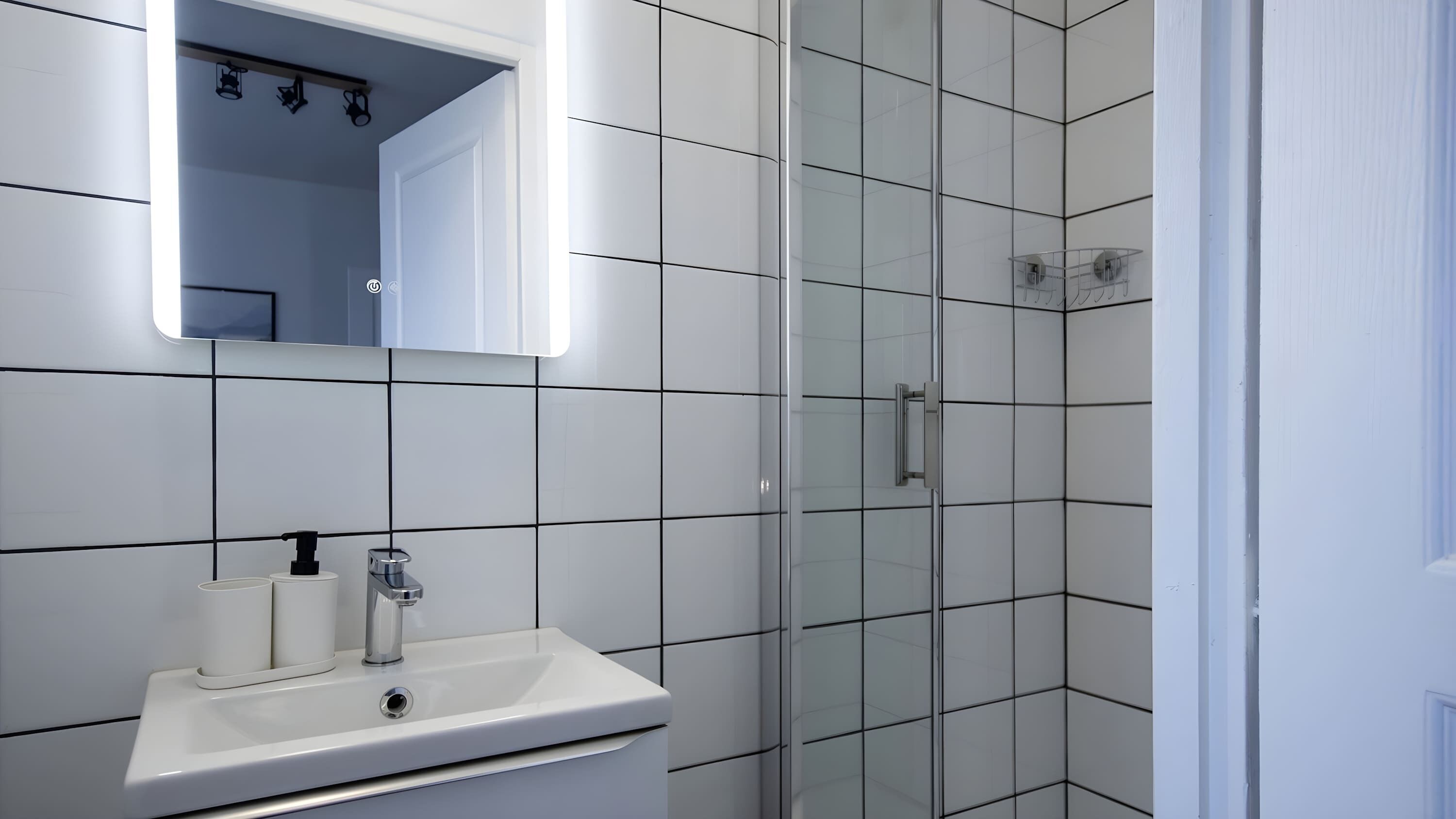 Ein modernes Badezimmer mit einem weißen Waschbecken, einem Spiegel und gefliesten Wänden.
