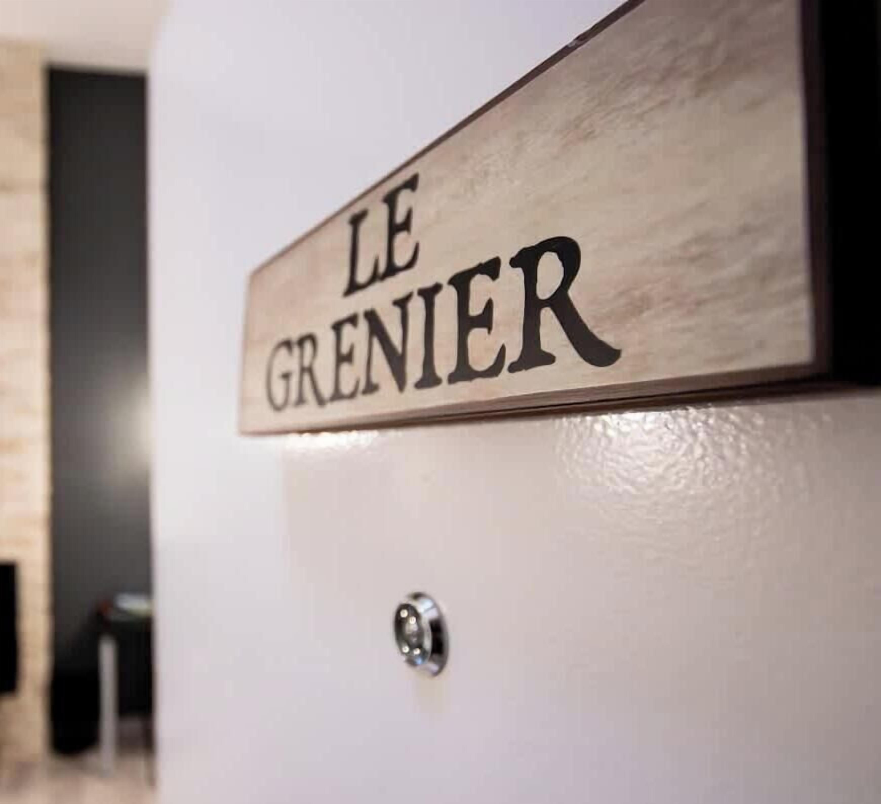 Een houten bordje met de tekst 'LE GRENIER' op een witte muur.