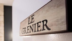 Een houten bordje met de tekst 'LE GRENIER' op een witte muur.