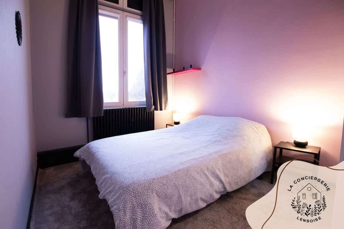 Un dormitorio con una cama, dos mesitas de noche, una ventana con cortinas y una lámpara de pared.