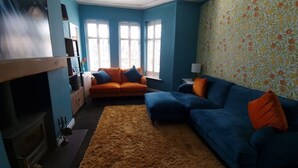 A living room with a blue sofa, orange cushions, a brown rug, and a fireplace. - Gorgeous Edwardian Terrace (Stretford)