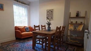 A living room with a wooden dining table, chairs, a sofa, a patterned rug, a potted plant, and a shelf with decorative items. - Gorgeous Edwardian Terrace (Stretford)