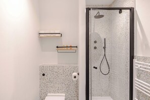 Moderni kylpyhuone, jossa on suihku, wc ja hylly, jossa on hygieniatuotteita.