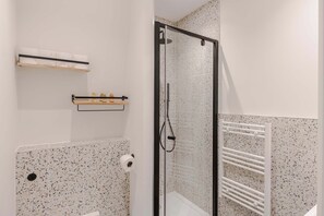 Eine Dusche mit Glastür, ein Handtuchhalter und ein Toilettenpapierhalter an der Wand.