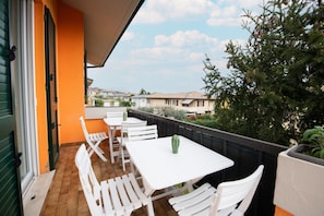 An outdoor patio with white tables and chairs, a potted plant, and a view of neighboring houses.