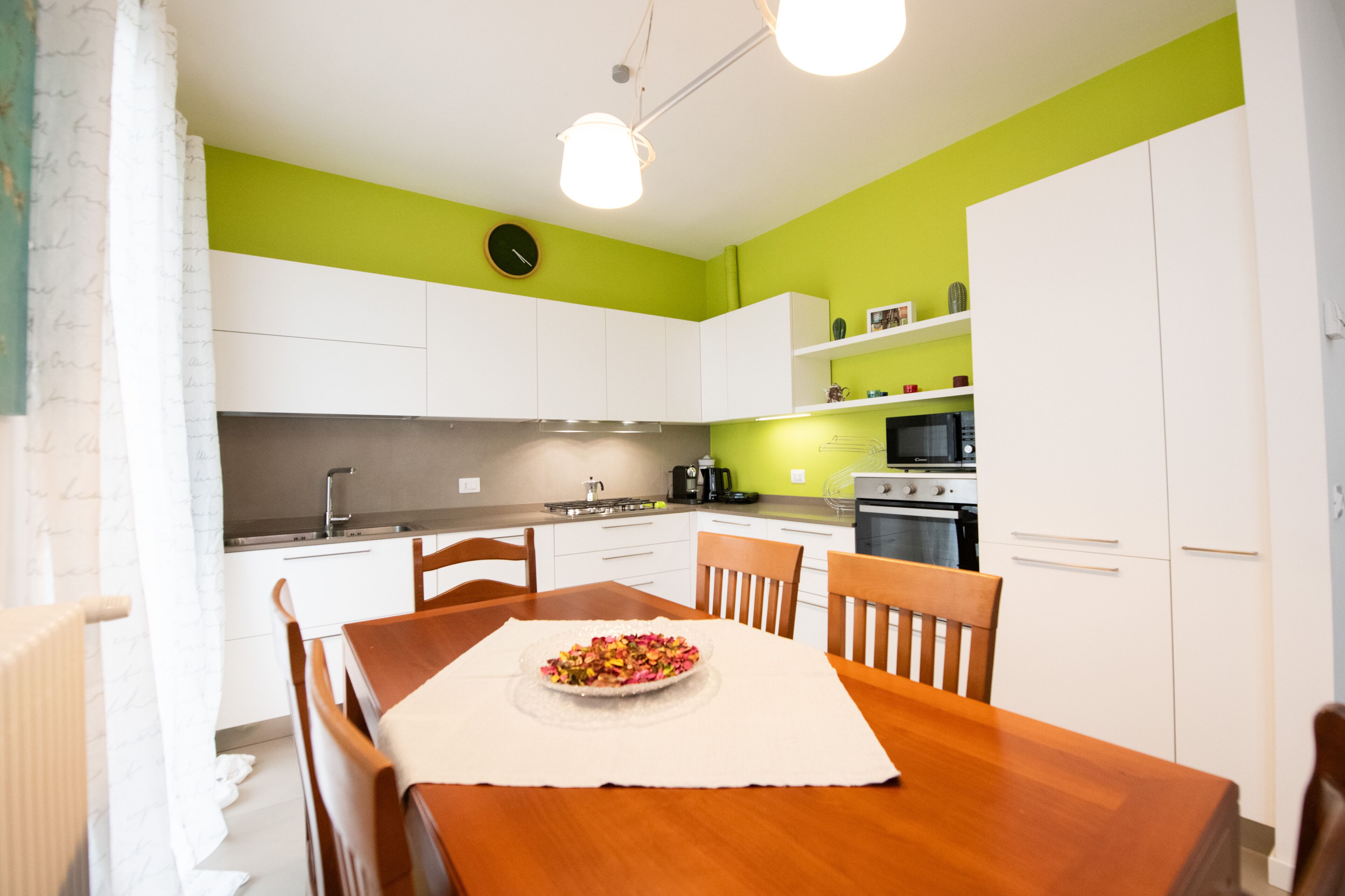 Une cuisine moderne avec des meubles blancs, une table à manger avec des chaises et une horloge au mur.
