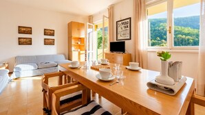 A dining area with a wooden table, chairs, and a TV. There are framed pictures on the wall and a window with a view of trees. - Peaceful Apartment With Terrace In Deiva Marina (Deiva Marina)