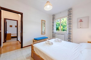 Un dormitorio con cama, ventana con cortinas, mesita de noche y lámpara.