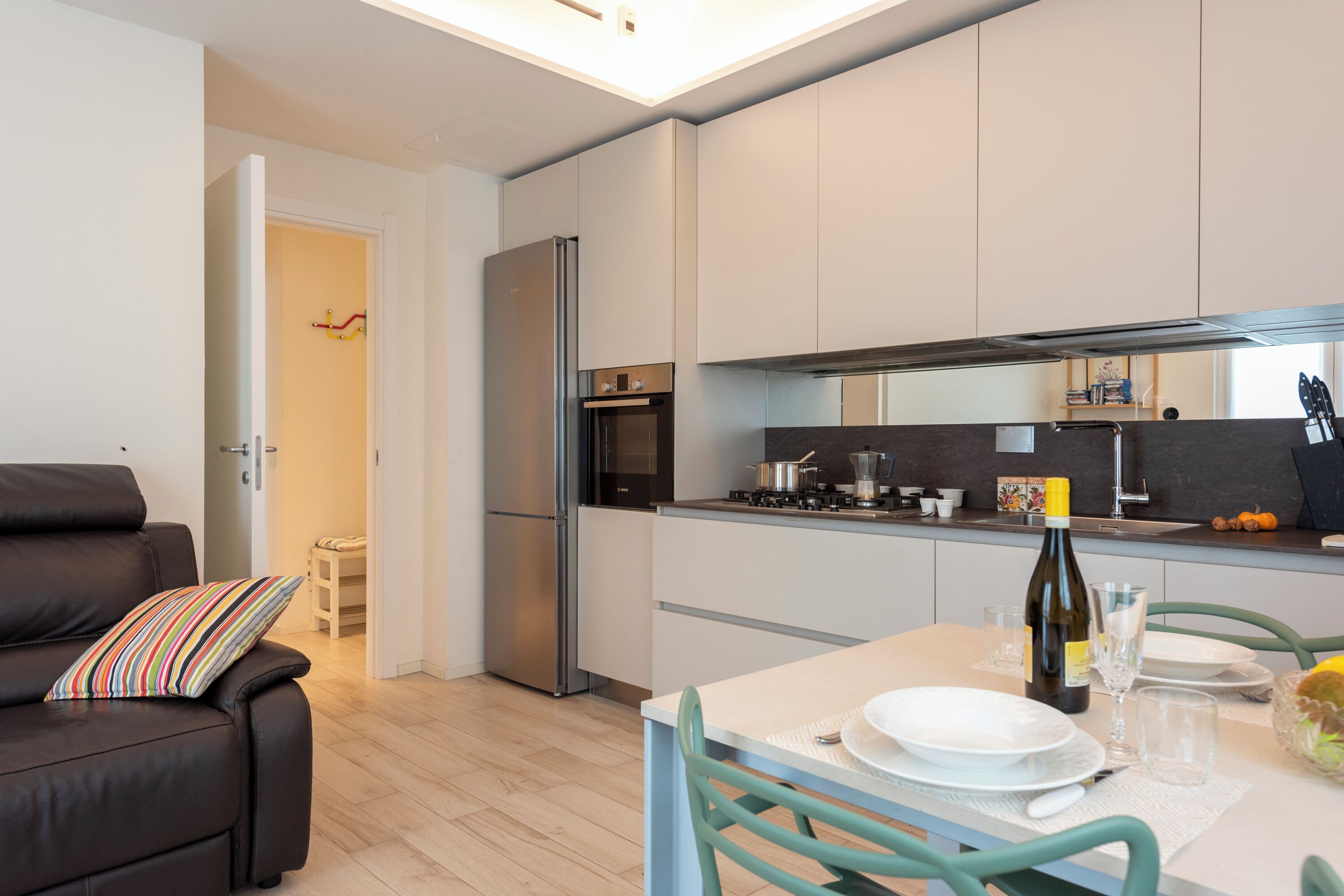 A modern kitchen with a dining area, featuring a sofa, a table set for two, and a refrigerator.