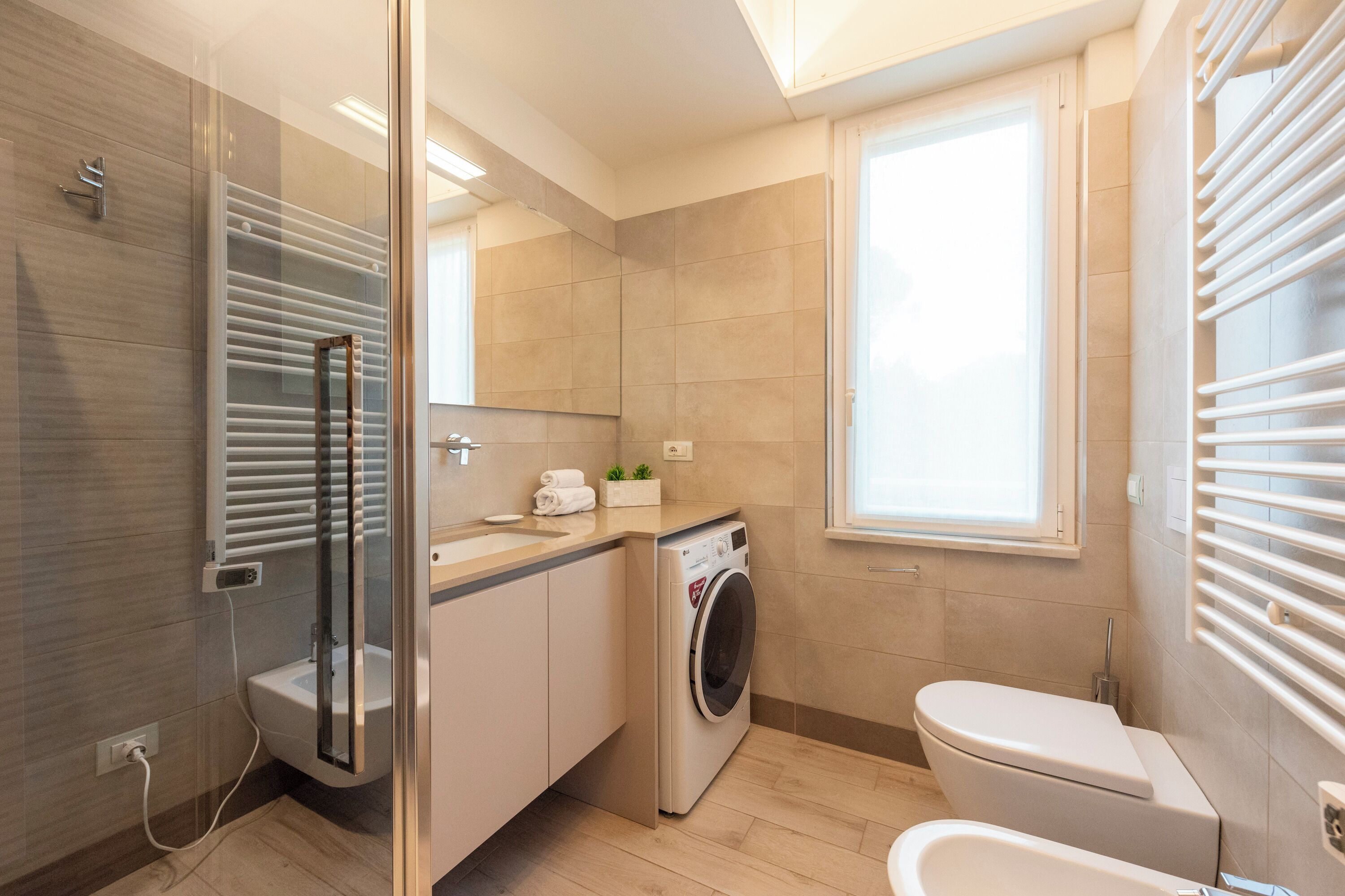 A modern bathroom with a glass shower enclosure, a built-in washing machine, and a toilet.