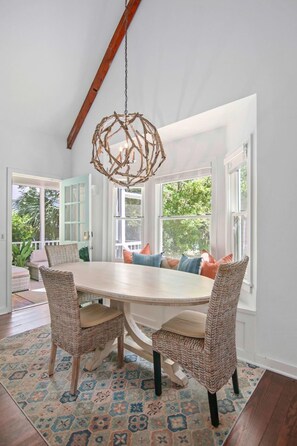 Uma área de refeições com uma mesa redonda, cadeiras de vime e um lustre singular.