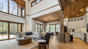 A spacious living area with a large sofa, a coffee table, and a dining table with chairs. There is a kitchen area with white cabinets and a wooden ceiling. - *Blue Turtle*Lux~Lake~Outdoor Life~Bike~Kayak~Dogs (Blue Ridge)