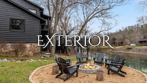A cabin with a fire pit and outdoor seating, surrounded by a stone wall and a pond.