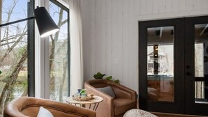A cozy room with a brown leather sofa, a round table with a plant, and a large window providing a view of the outdoors.