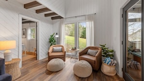 A cozy living room with wooden floors, two leather armchairs, a small round table, and a large window with curtains.