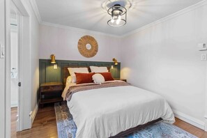 Un dormitorio con cama, mesitas de noche, lámpara de pared y un espejo decorativo.