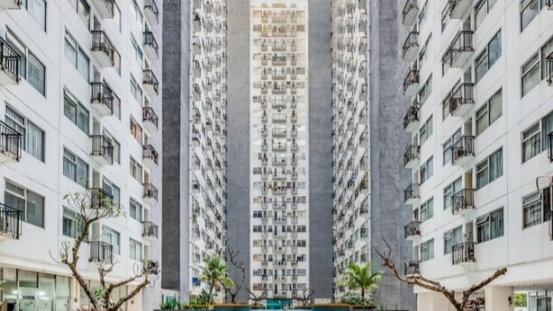 A high-rise residential building with multiple balconies, a central courtyard with a pool, and surrounding greenery.
