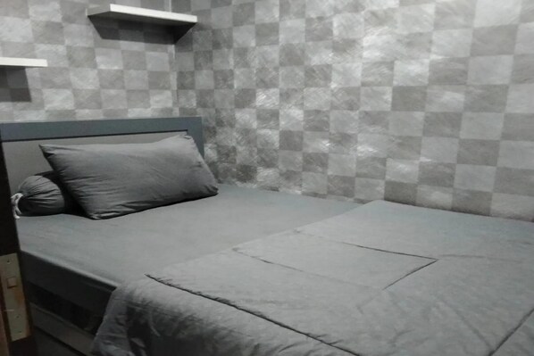 A single bed with a grey mattress and pillows, a wooden headboard, and a checkered wall pattern. - Hotel O The Jarrdin Apartment By Yedi Property (Bandung)