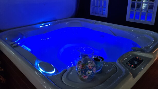 A hot tub with a blue light, a floral vase, and a cup on a tray. - Dungarvon House B&B (Weston-super-Mare)