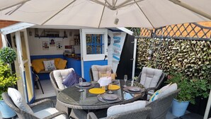 An outdoor patio with wicker furniture, a round glass table, and a covered seating area. - Dungarvon House B&B (Weston-super-Mare)