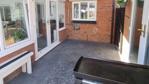A covered patio with a bench, a water feature, and a view of the garden through glass doors. - Dungarvon House B&B (Weston-super-Mare)