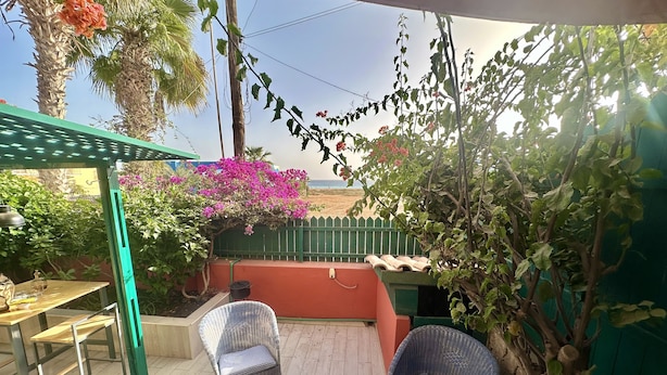 Un patio al aire libre con sillas de mimbre, una mesa y vista a la playa.