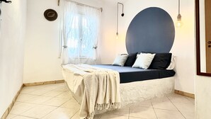Un dormitorio con cama, ventana con cortinas, luz empotrada en la pared y una bombilla colgante.