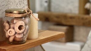 Un baño con pared de mármol, un estante de madera con un tarro de toallas dobladas y una vela blanca.