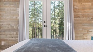 Une chambre avec un grand lit, des murs en bois et une vue sur les arbres, visible à travers une porte vitrée.