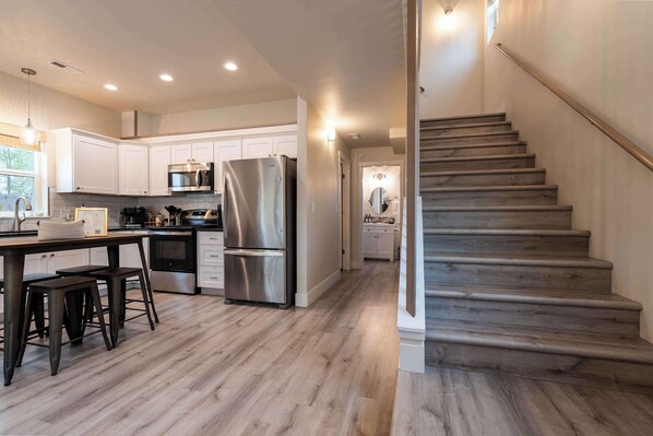 A modern kitchen with white cabinets, stainless steel appliances, and a wooden staircase.