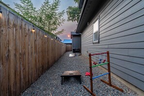 A backyard with a wooden fence, a small wooden table, a metal swing set, and a house with a window.