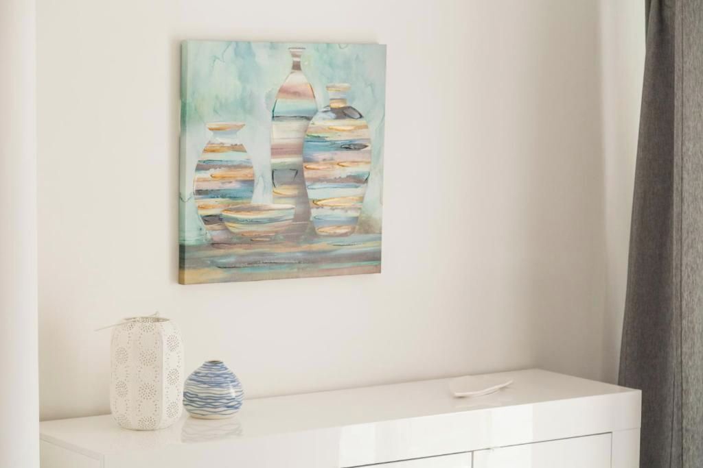 A painting of bottles on a wall, a white cabinet with two vases, and a window with curtains.