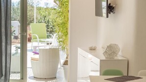 Une chambre moderne dotée d’une porte-fenêtre coulissante donnant sur un espace extérieur, d’un fauteuil en osier blanc, d’un bureau blanc avec un ordinateur et d’un objet décoratif en verre posé sur le bureau.