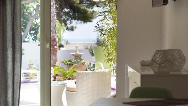 Une pièce donnant sur un jardin, avec un fauteuil en osier blanc, une chaise verte et une petite table agrémentée d’un objet décoratif.