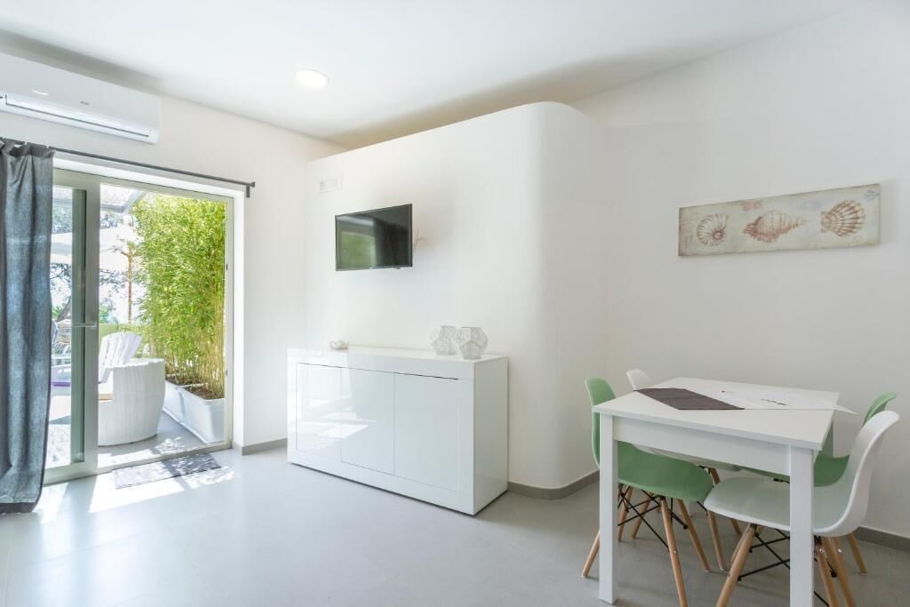 Une pièce moderne et minimaliste, avec un bureau blanc et des chaises vertes, un téléviseur à écran plat fixé au mur et une fenêtre donnant sur un paysage verdoyant.