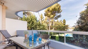 Un balcón con mobiliario de mimbre, una mesa de vidrio y vistas a un jardín y piscina.