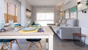 Una sala de estar moderna con comedor, que incluye un sofá, una mesa baja y una mesa de comedor con platos y vasos.