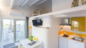 Cocina compacta con televisor, comedor con mesa y sillas, y balcón con mobiliario de exterior.