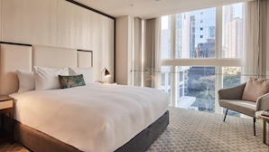 A modern hotel room with a large bed, a sitting area with a sofa, a desk, and a view of the city through large windows. - The Inchcolm by Ode Hotels (Spring Hill)