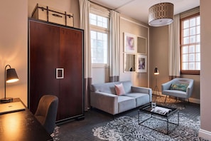 Una habitación de hotel moderna con un sofá gris, una mesita, un escritorio con lámpara, una silla y un armario grande.