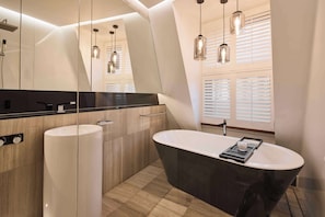 Un baño moderno con una bañera independiente, un espejo grande e iluminación colgante.