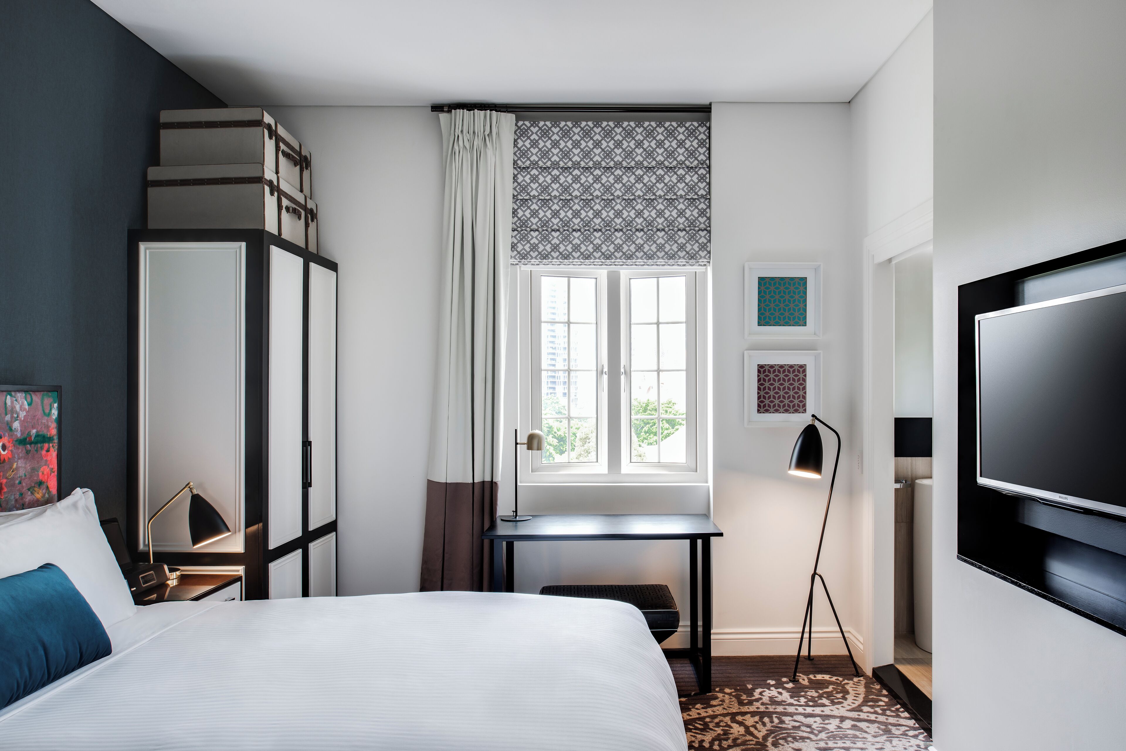 A hotel room with a bed, a desk, a TV, and a window with curtains.