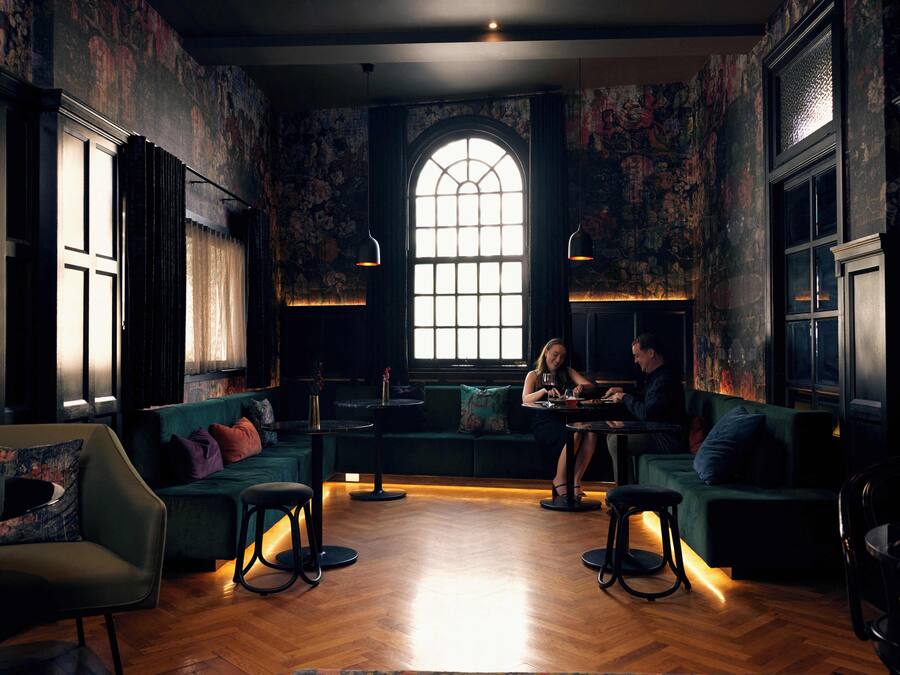 Un espace salon accueillant, avec des canapés verts, un plancher en bois et une grande fenêtre en arc de cercle qui laisse entrer la lumière naturelle.