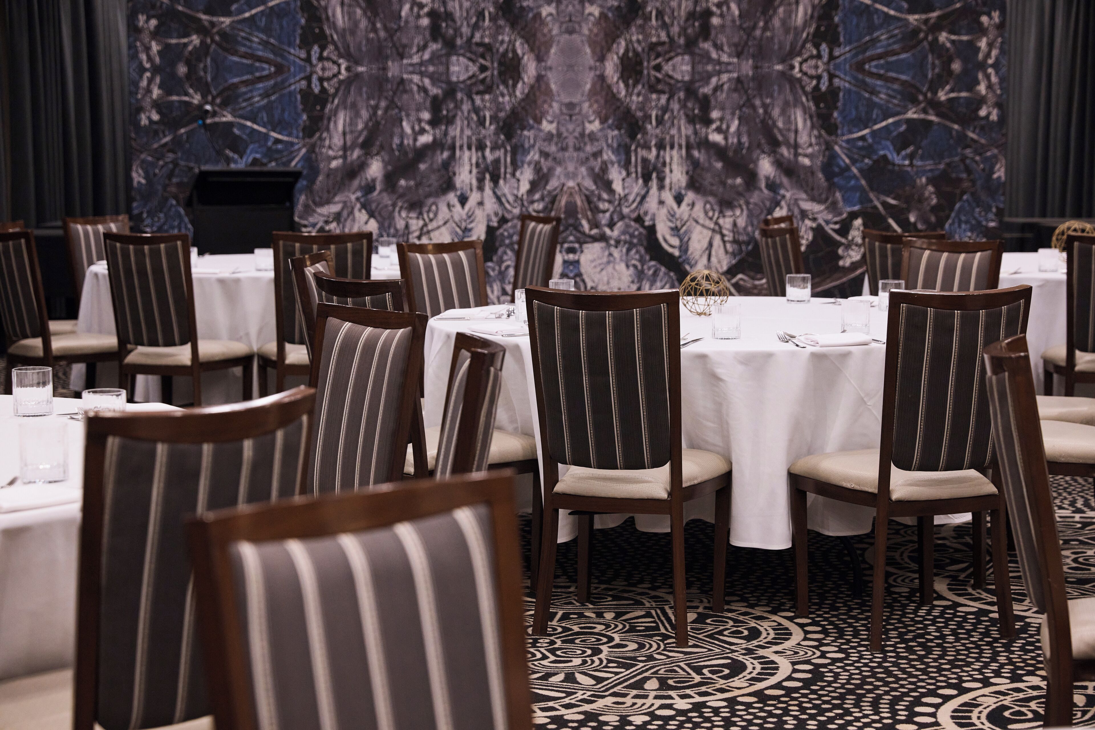 Un comedor con sillas a rayas y mesas redondas, frente a un papel tapiz estampado.