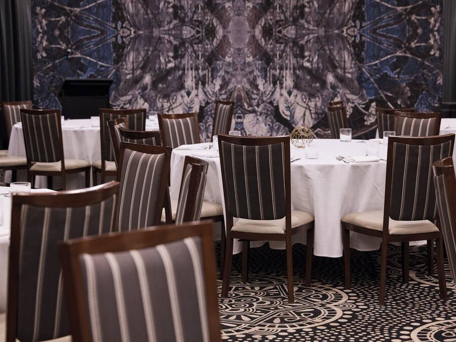 Un comedor con sillas a rayas y mesas redondas, frente a un papel tapiz estampado.