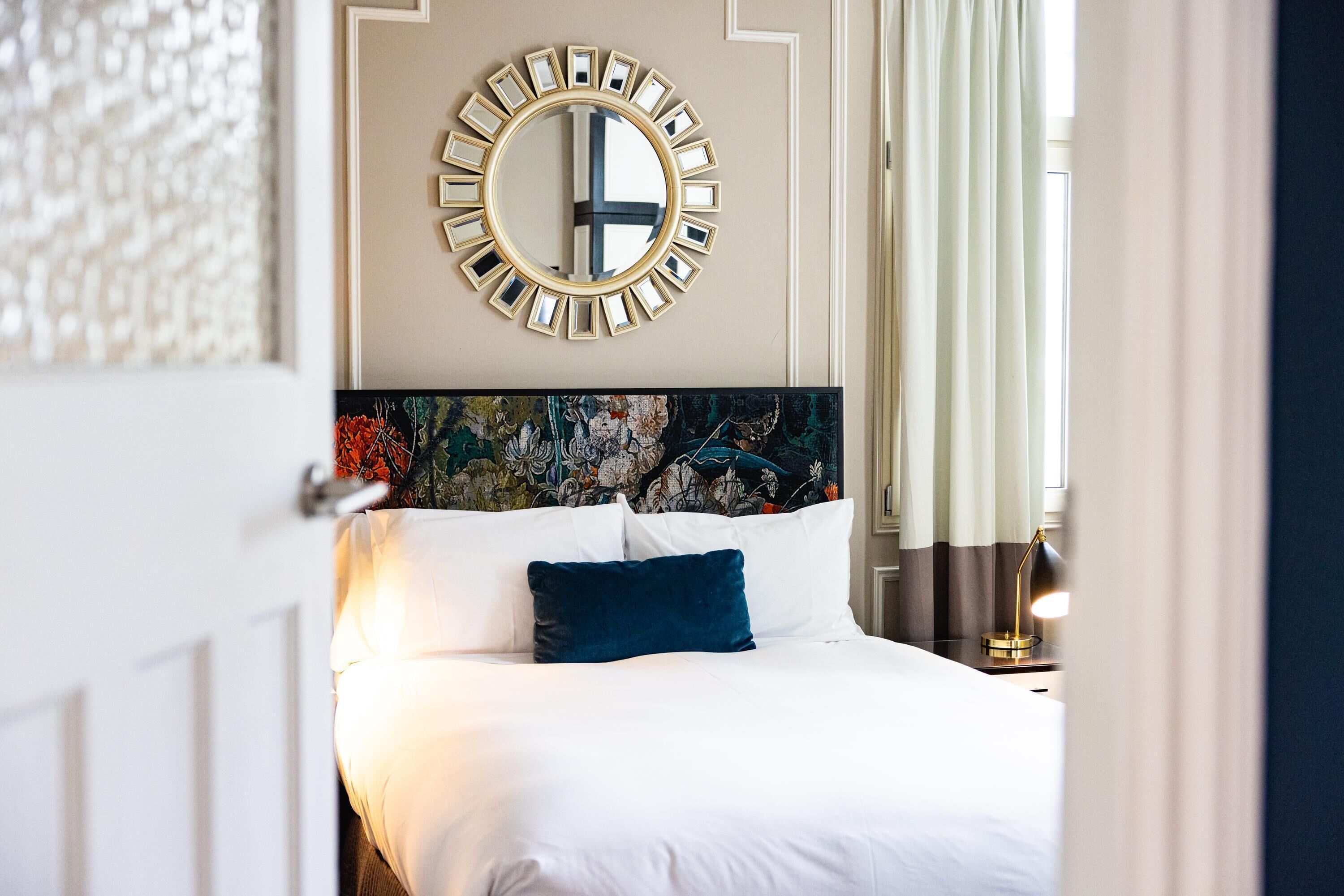 A hotel room with a bed, a round mirror, and a floral headboard.